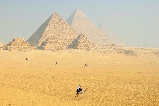 A person on a camel while admiring the pyramids of Egypt